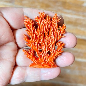 May include: A vibrant orange coral sculpture with intricate details. The coral is a bright, glossy orange, and the design mimics the natural structure of coral reefs. The sculpture is held in a hand, showcasing its size and form.