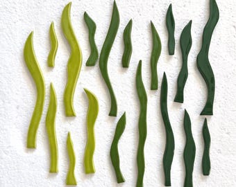 May include: A collection of seventeen individual ceramic wall tiles shaped like wavy, elongated blades of grass or seaweed. The tiles feature a glossy finish in varying shades of green, ranging from bright lime to deep forest green.