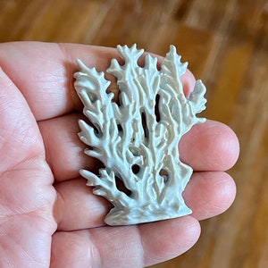 May include: A white ceramic coral sculpture with intricate details. The sculpture has a textured surface and a glossy finish. The coral is held in a hand, showcasing its size and form. The piece is likely a decorative item.