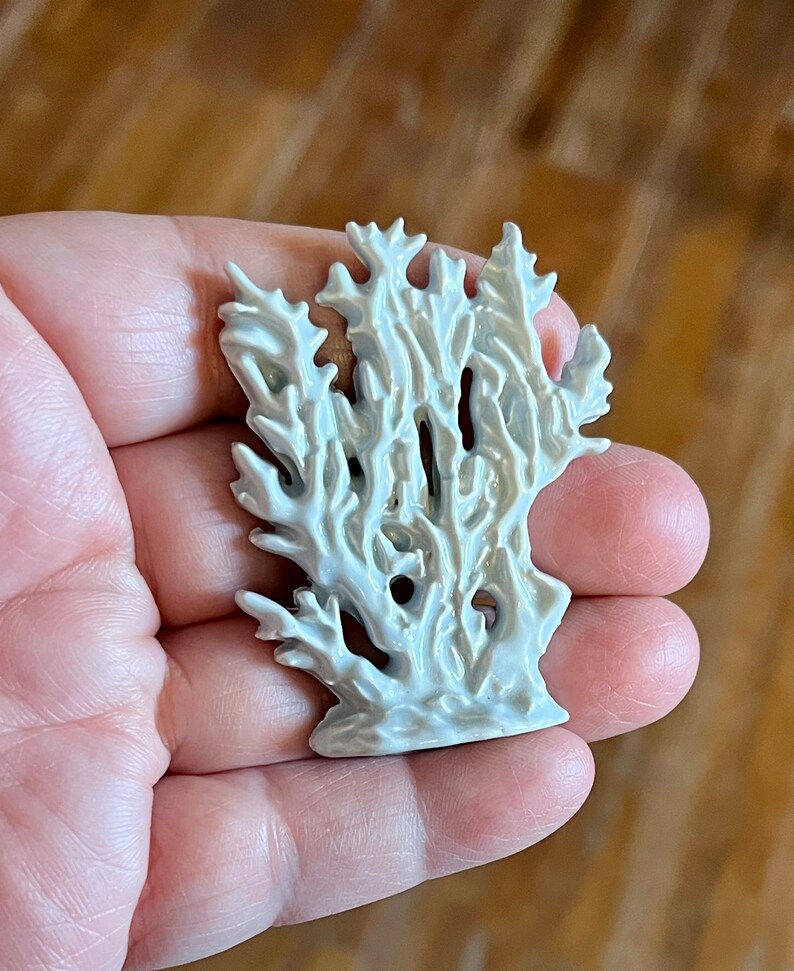 May include: A white ceramic coral sculpture with intricate details. The sculpture has a textured surface and a glossy finish. The coral is held in a hand, showcasing its size and form. The piece is likely a decorative item.