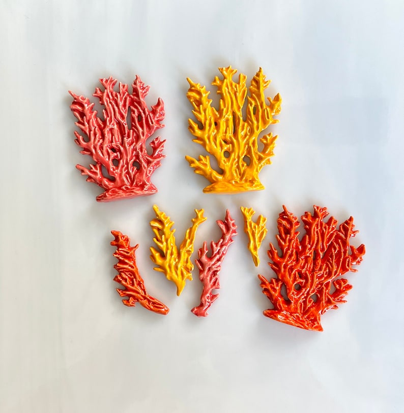 May include: A collection of coral-shaped decorative objects in various shades of red, orange, and yellow. The objects have a textured surface and are arranged on a white background. These decorative pieces are ideal for coastal or nautical-themed decor.
