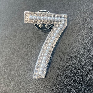 May include: A silver-toned number seven pin with white pearl accents.