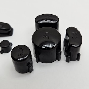 May include: Set of five black replacement buttons for a game controller. The buttons are labeled A, B, X, and Y.