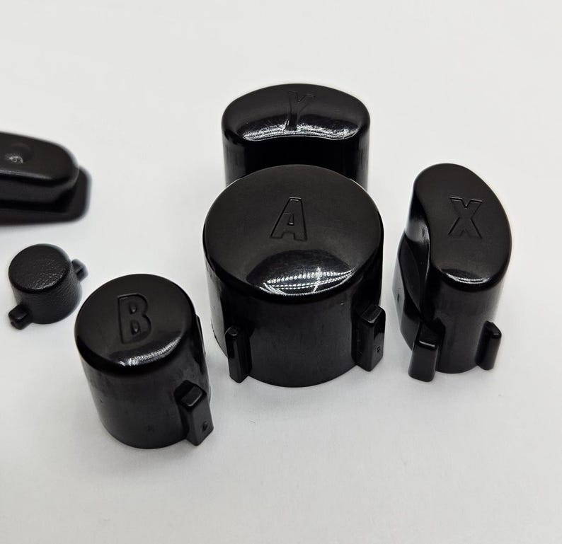 May include: Set of five black replacement buttons for a game controller. The buttons are labeled A, B, X, and Y.