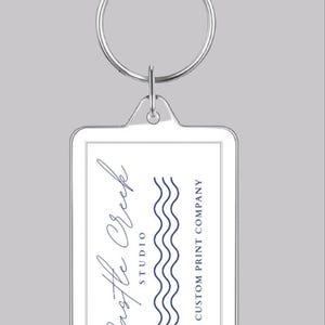 May include: A white rectangular keychain with a silver ring. The keychain has a blue wave design and the text "Castle Creek Studio A Custom Print Company".