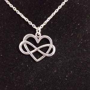 May include: Silver necklace with an infinity symbol intertwined with a heart pendant.