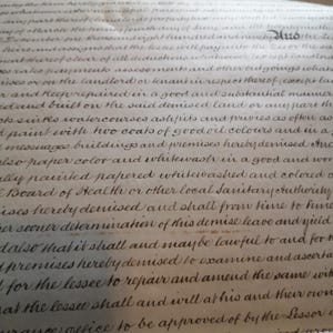 May include: Close-up of an antique document featuring handwritten cursive script. The aged paper has a cream hue, and the ink is dark brown. The text appears to be legal or historical, with visible words and phrases.