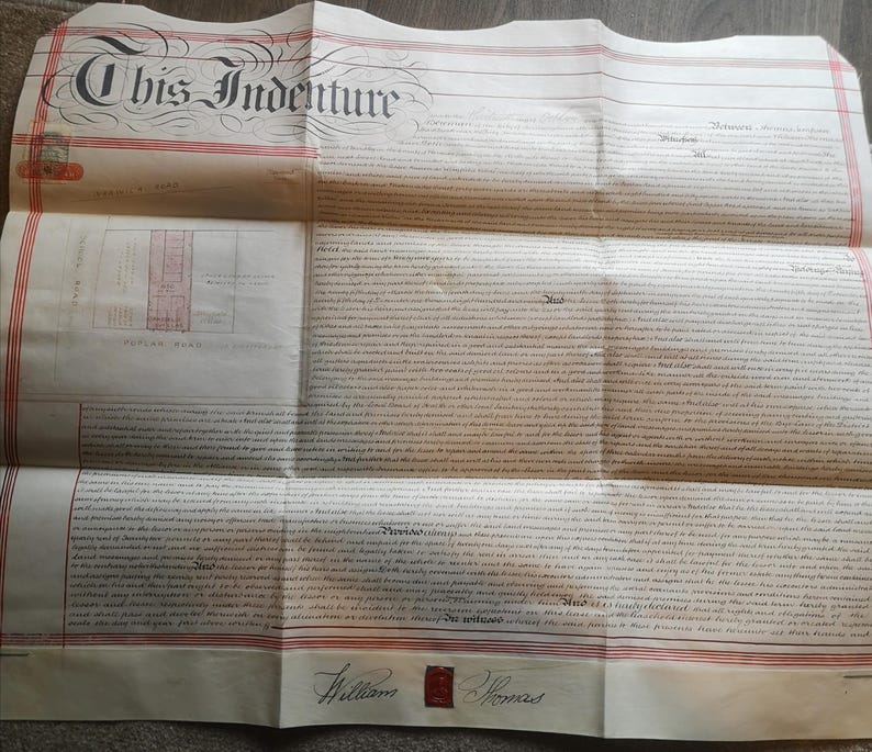 May include: An antique document titled "This Indenture" with ornate calligraphy. The paper is aged, with red stripes and text throughout. A small map and signatures are visible. The document is folded.