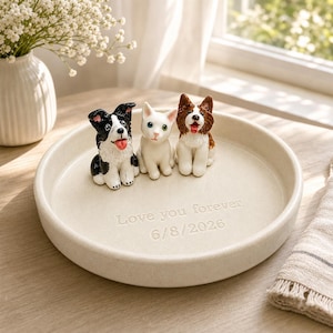 May include: A round, off-white ceramic trinket dish featuring three small animal figurines: a black and white dog, a white cat, and a brown and white dog. The dish is engraved with the text "Love you forever" and the date "6/8/2026" in the center.