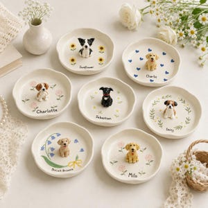 Puede incluir: Siete platos de cerámica redondos, cada uno con una pequeña figura de perro en 3D en el centro. Los platos están decorados con motivos florales o de corazones e incluyen los nombres Sunflower, Charlie, Charlotte, Sebastian, Daisy, Biscuit Brownie y Milo.