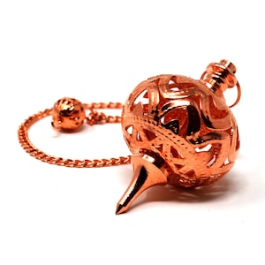 May include: A copper pendulum with a delicate, intricate design. The pendulum has a pointed tip and a round, openwork ball. It is attached to a chain with a small ball at the end.
