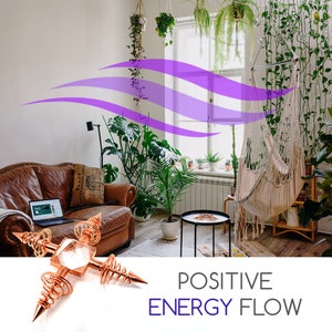 May include: A copper orgonite pyramid with a clear quartz crystal in the center. The pyramid is surrounded by copper wire coils and has four copper spikes extending from the corners. The pyramid is sitting on a white surface. The image also shows a living room with a couch, plants, and a hammock. The text "POSITIVE ENERGY FLOW" is written in purple letters below the pyramid.