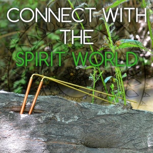 May include: Two gold-colored metal rods are placed on a brown tree trunk. The rods are bent at the top and are positioned in a V-shape. The background is blurred and features green foliage and the text "CONNECT WITH THE SPIRIT WORLD".