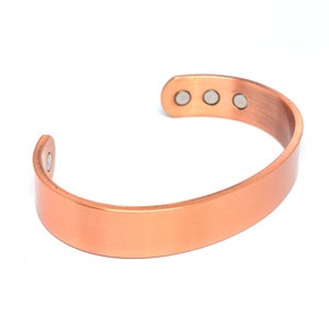 May include: A copper bracelet with four magnetic closures. The bracelet is smooth and has a polished finish.
