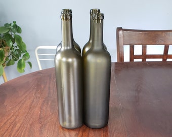 May include: Four dark green glass wine bottles with cork tops are lined up on a wooden table.