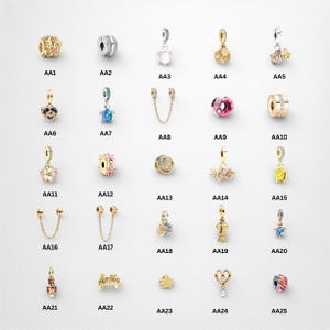 Peut inclure: Une collection de breloques dorées avec divers motifs, notamment floraux, géométriques et ornés de pierres précieuses. Certaines breloques comportent des éléments pendants, tandis que d'autres sont de simples perles. Les breloques sont disposées sur fond blanc.