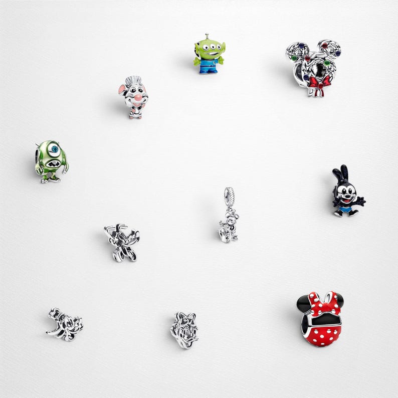 May include: A collection of ten silver-toned metal charms featuring various animated character designs, including a green alien, a one-eyed monster, a red polka-dot bow, a black and white rabbit, and other detailed miniature figures with enamel accents.