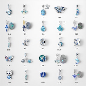 Può includere: Una collezione di venticinque ciondoli color argento etichettati da D1 a D25, con vari design a tema blu che includono creature marine, insetti, farfalle e motivi floreali, alcuni dei quali incorporano cristalli scintillanti e smalto.