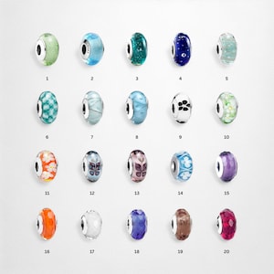 May include: A collection of twenty colorful glass beads with various designs. The beads are oval-shaped and feature a range of colors including green, blue, purple, orange, and brown. Some beads have floral or patterned details.