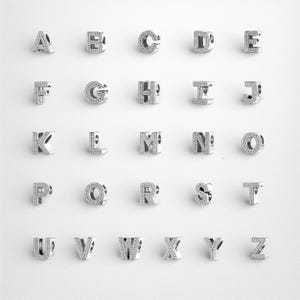 Może przedstawiać: Srebrne zawieszki z literami alfabetu, każda litera inkrustowana małymi, przezroczystymi kryształkami. Litery od A do Z są wyświetlane w siatce na białym tle. Te zawieszki nadają się do bransoletek lub naszyjników.