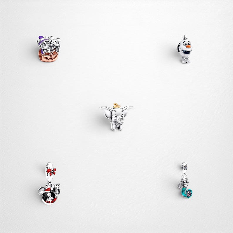 May include: A collection of five silver charms featuring various characters. Included are a pumpkin-themed charm with a purple hat, a snowman figure, a small elephant with large ears, a holiday-themed mouse charm, and a mermaid-inspired charm.