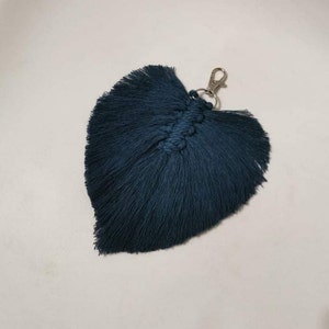 May include: A dark blue feather keyring with a silver metal clasp. The feather is made of yarn and has a fringed edge.