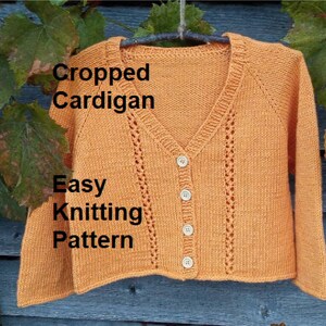 May include: A cropped cardigan knitting pattern with a V-neck and button fastening. The cardigan is a light orange colour and has a lacy stitch pattern. The text "Cropped Cardigan Easy Knitting Pattern" is visible in the image.