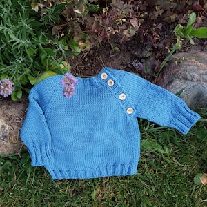 May include: A blue knitted sweater with a round neckline and button detailing on the shoulder.