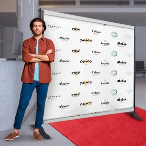 May include: A white backdrop with a repeating pattern of various logos, including "rosé", "hipster", "Saturday", "Urban", "Iconic", "Happy", "Everyday", and "Mockup". A person is standing in front of the backdrop.