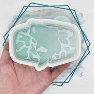 May include: A light blue rectangular resin mold with a fish design. The mold has a white border and is held in a hand. The fish design is surrounded by a mottled pattern. The mold is on a white surface with a teal geometric design.