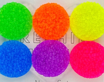 May include: A set of six neon-colored, circular objects. The colors include green, orange, yellow, blue, purple, and pink. The text "Neon Set" is displayed at the bottom. The objects have a textured, bumpy surface.