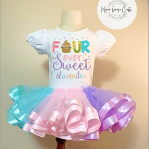 May include: A white short-sleeved shirt with the text "FOUR ever Sweet Lavender" and a cupcake graphic. The shirt is paired with a multi-colored tulle skirt with pink, blue, and purple ribbon accents.