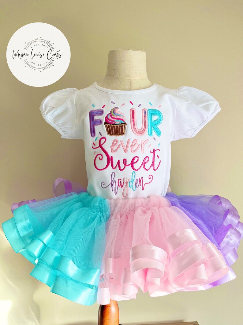 May include: A white short-sleeved shirt with the text "FOUR ever sweet hayden" and a cupcake graphic. The shirt is paired with a multi-layered tulle skirt in shades of pink, blue, and purple.