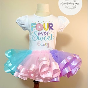 May include: A white short-sleeved shirt with a donut graphic and the text "FOUR ever Sweet Casey" on it. The shirt is paired with a multi-colored tulle tutu with pink, blue, and purple ribbon accents.