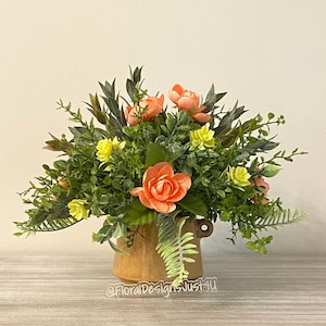 May include: A floral arrangement in a brown ceramic vase. The arrangement features peach-colored flowers and green foliage.