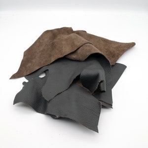 Könnte beinhalten: Ein Stapel brauner und schwarzer Lederreste. Das Leder ist weich und geschmeidig, und die Kanten sind leicht ausgefranst.