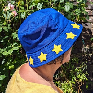 May include: A blue bucket hat with yellow stars around the brim. The hat is made of a soft, textured fabric.