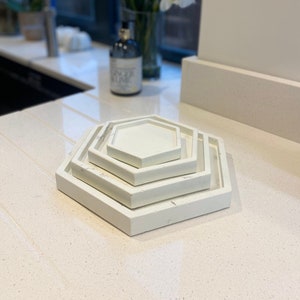 May include: A set of three white hexagonal trays, stacked on top of each other. The trays are made of a textured material and have a slightly distressed look.