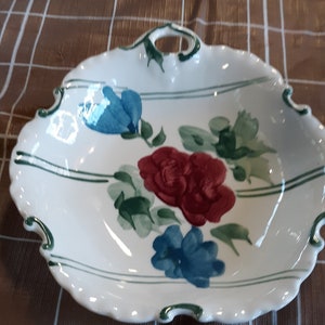 May include: White ceramic serving dish with a scalloped edge and a handle. The dish is decorated with red and blue floral designs and green accents. The dish has a diameter of approximately 10 inches.
