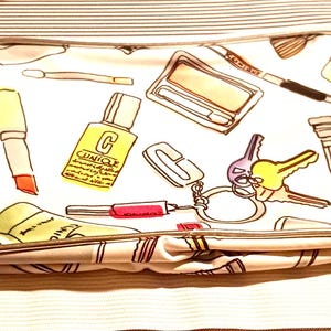 May include: White cosmetic bag with a pattern of makeup items, including lipsticks, brushes, and Clinique bottles. The bag also features a set of keys on a keychain. The bag is closed and has a zipper.