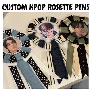 May include: Three custom KPOP rosette pins. Each pin features a photo of a person, surrounded by decorative ribbons and embellishments. The ribbons are in various colors, including black, white, and denim blue, with polka dot and striped patterns.