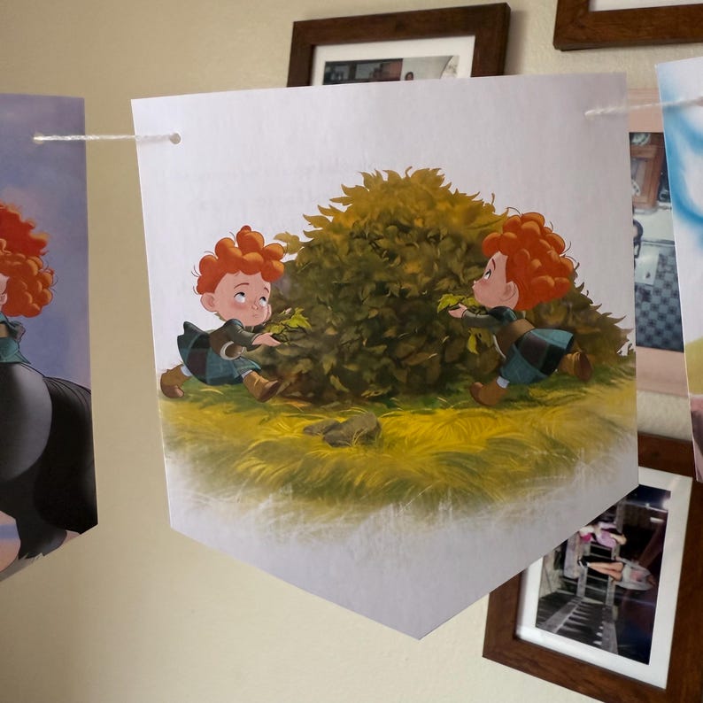 Peut inclure: Une banni&egrave;re en forme de fanion avec une illustration de deux enfants aux cheveux roux boucl&eacute;s jouant pr&egrave;s d'un buisson vert. Ils portent des tenues bleues et vertes. La banni&egrave;re est suspendue &agrave; un mur avec une ficelle blanche.