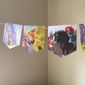 Peut inclure: Une guirlande de fanions illustr&eacute;s tir&eacute;s d'un film pour enfants. Les fanions sont reli&eacute;s par une ficelle blanche. Les illustrations repr&eacute;sentent une jeune fille rousse dans diverses sc&egrave;nes, notamment en train d'escalader une falaise et de monter un cheval noir.