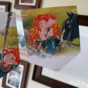 Peut inclure: Guirlande de fanions illustr&eacute;s tir&eacute;s d'une histoire pour enfants. Les fanions repr&eacute;sentent un personnage roux avec trois autres personnages et un cheval noir. Les fanions sont reli&eacute;s par une ficelle blanche.