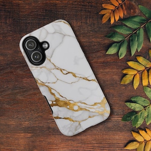May include: White and gold marble-patterned phone case with a black camera module. The case features a veined design in gold against a white background. The phone case is on a dark wooden surface, with green and yellow leaves.