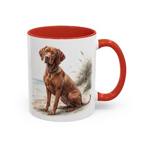 Può includere: Tazza in ceramica bianca con interno e manico rossi. La tazza presenta un'illustrazione ad acquerello di un cane marrone seduto su una spiaggia sabbiosa. Il cane indossa un collare grigio.