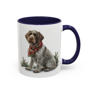 Peut inclure: Mug en céramique blanche avec intérieur et anse bleu marine. L'illustration détaillée représente un chien portant une écharpe rouge et verte. Le chien est assis dans une scène enneigée avec de petits arbres.