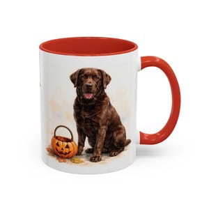 Pode incluir: Uma caneca de cerâmica branca com interior e alça em vermelho brilhante. O exterior apresenta uma ilustração detalhada de um labrador retriever castanho sentado ao lado de um pequeno balde de abóbora laranja num fundo claro.