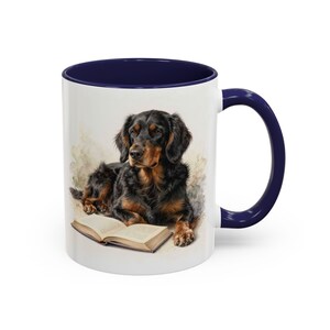 May include: White ceramic mug with a navy blue interior and handle. The mug features a watercolor illustration of a black and brown dog lying next to an open book. The dog is the primary focus of the design.