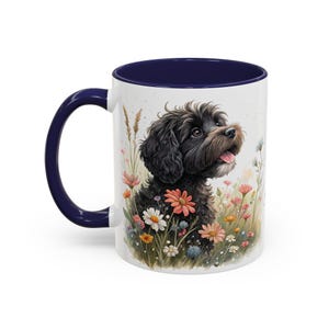 Puede incluir: Una taza de cerámica blanca con un borde y un asa azul marino. La taza presenta una ilustración en blanco y negro de un perro pequeño con una expresión feliz, rodeado de flores coloridas.